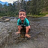child, boy, water, river, nature, outdoor, forest, trees, sky, clouds, rocks, greenery, shallow_water, playing, smiling, crouching, summer, casual_clothing, daytime, fun