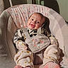 baby, infant, smiling, baby_rocker, floral_pattern, pink_socks, cozy, cute_outfit, happy, indoors, soft_lighting, child, face, person, seated, baby_clothes, comfort, home, small_child, adorable