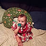 baby, child, infant, smiling, sitting, bed, blanket, pillow, toy, pacifier, dress, red_clothing, floral_pattern, indoor, cute, face, person, happy, playful, home