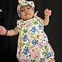 baby, blue, cartoon_print, child, colorful_clothing, cute, expression, face, green, headband, indoors, infant, lying_down, mittens, onesie, palm_tree, person, pink, starfish, yellow