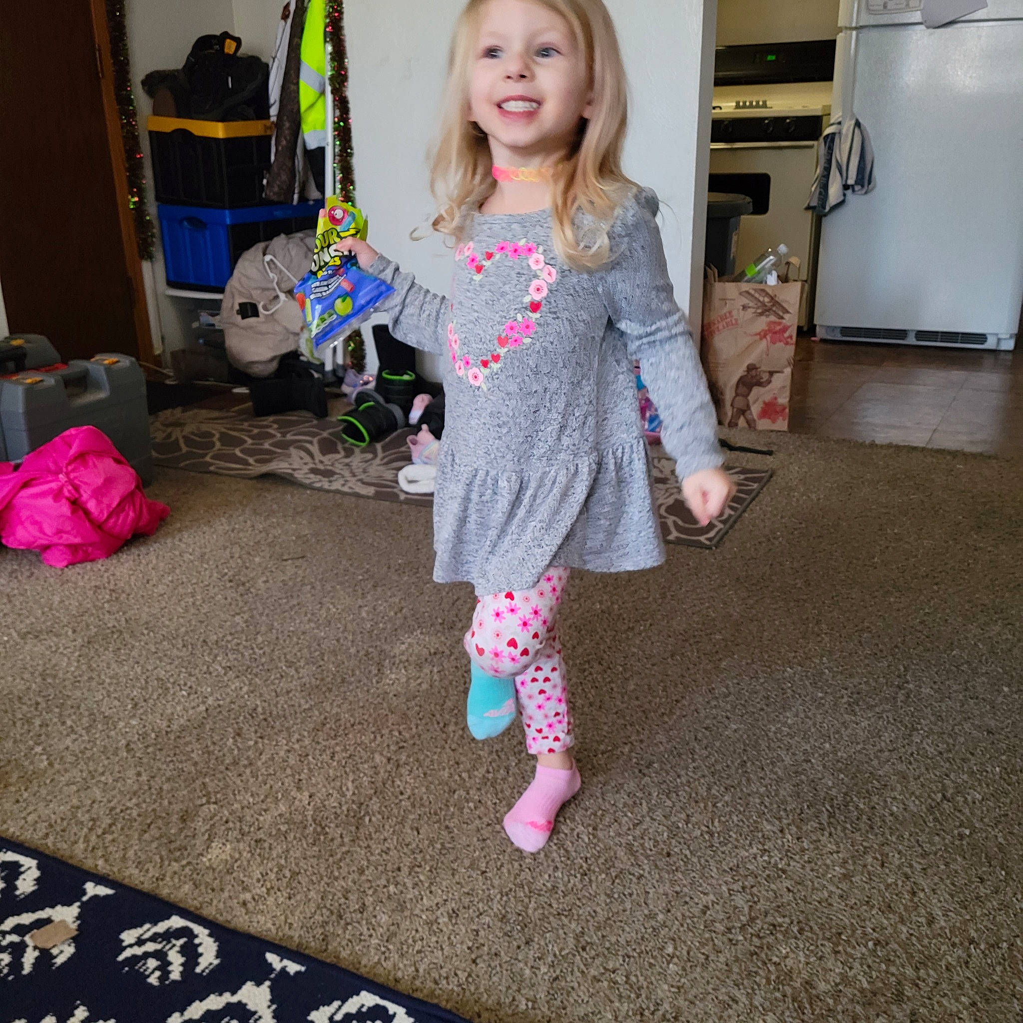 Keira is registered to the contest to win money with this photo: baby_toddler_clothing, child, dress, eye, face, fashion_design, floor, flooring, joy, kitchen_appliance, magenta, one_piece_garment, pattern, person, pink, refrigerator, room, sleeve, smile, sock