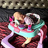 baby, infant, walker, toy, sleeping, bed, patterned_bedspread, headboard, pink, purple, blue, clothing, foot, face, indoor, child, resting, furniture, cute, toddler