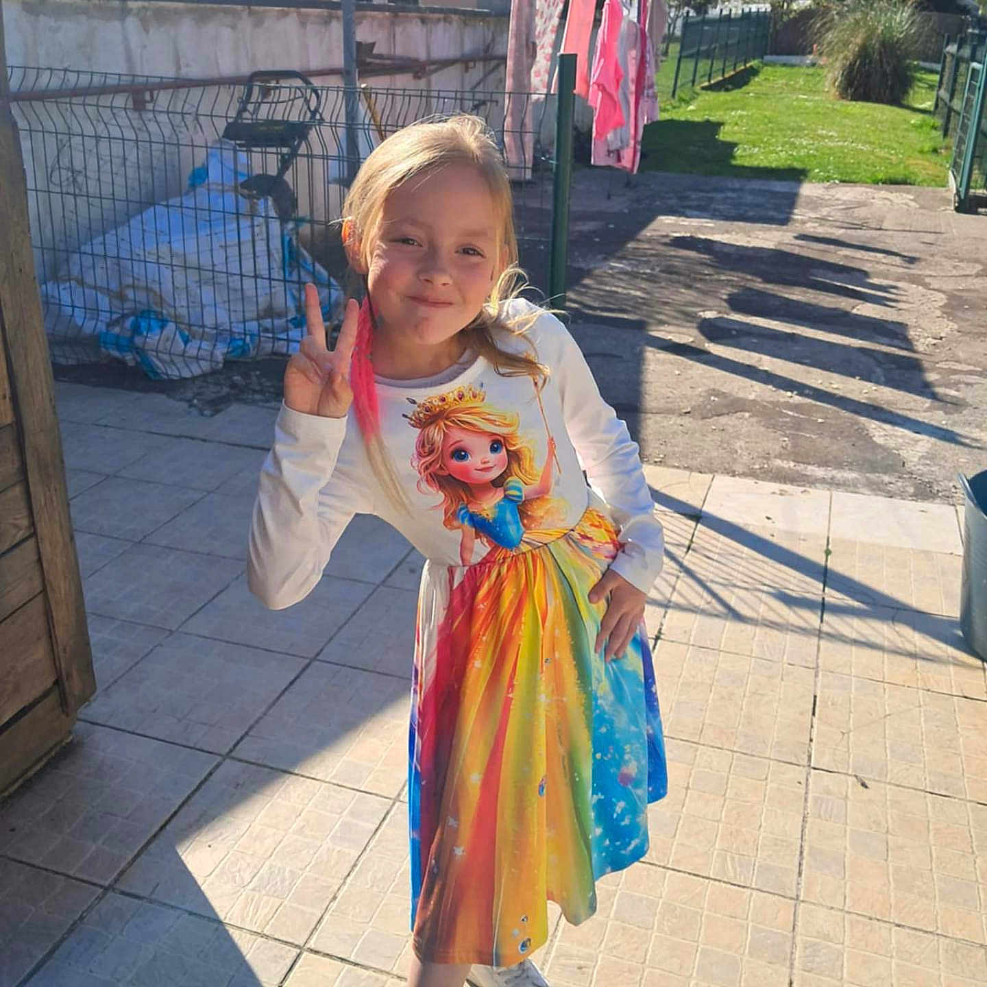 Cristal a rejoint le concours — aidez-le/la à gagner de superbes lots ! casual_pose, child, colorful_dress, daytime, fence, girl, grass, happy, laundry, outdoor, peace_sign, playful, princess_print, shadow, smile, sunlight, tile_floor, tree, white_shoes, young