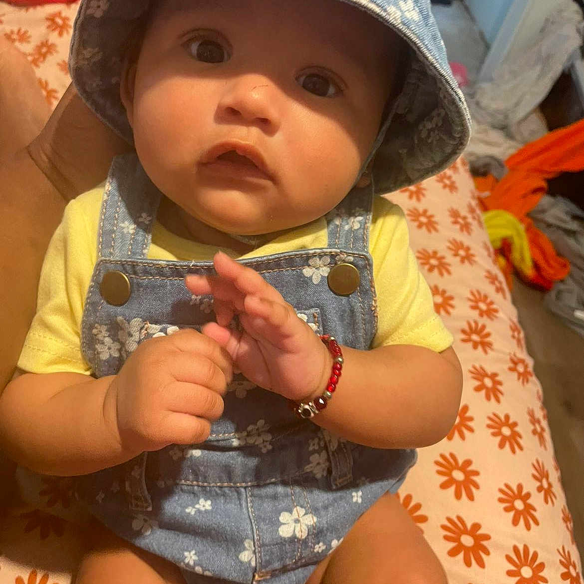 Eliana is registered to the contest to win money with this photo: baby, bed, blanket, bracelet, child, clothing, cute, denim, flower, hand, hat, indoor, orange, overalls, pattern, person, portrait, skin, yellow, young