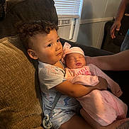 Kason is registered to the contest to win money with this photo: child, baby, couch, curly_hair, sleeping, holding, indoor, window, air_conditioner, pacifier, tattoo, pink_clothing, family, toddler, boy, newborn, love, care, soft_light, cozy