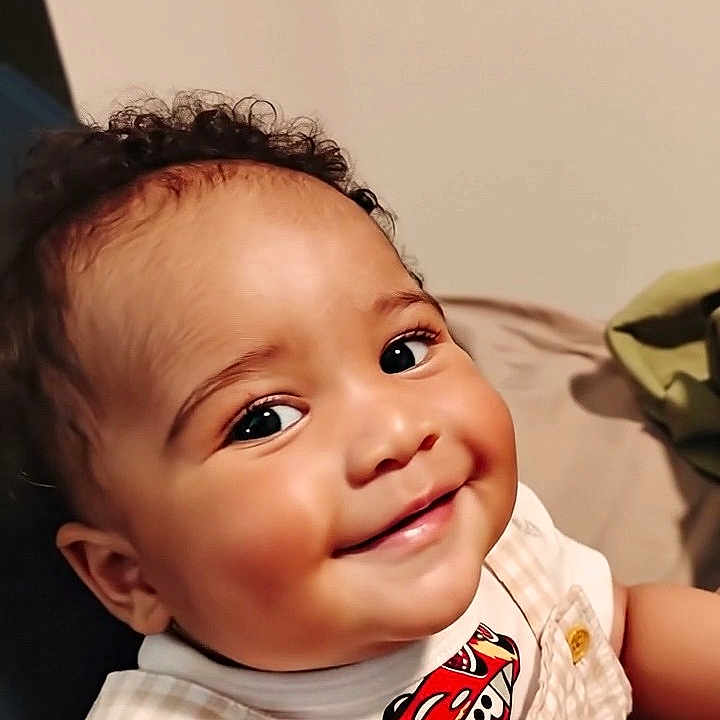 J'Khari is registered to the contest to win money with this photo: baby, child, smiling, face, curly_hair, clothing, cartoon_cars, portrait, indoor, cute, happy, infant, person, skin, toddler, cheeks, eyes, sitting, overalls, short_sleeves