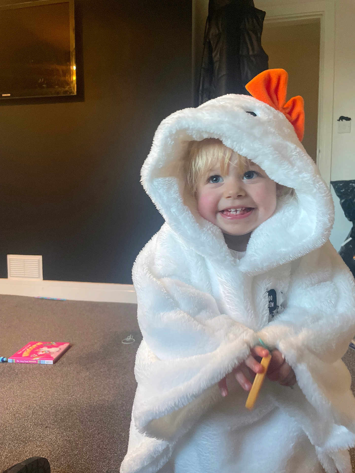 Nancy-Valentina is registered to the contest to win money with this photo: blond_hair, blue_eyes, book, carpet, child, clothing, costume, cozy, cute, happy, hood, indoor, orange_bow, person, room, small_object, smile, toddler, toy, white_fabric