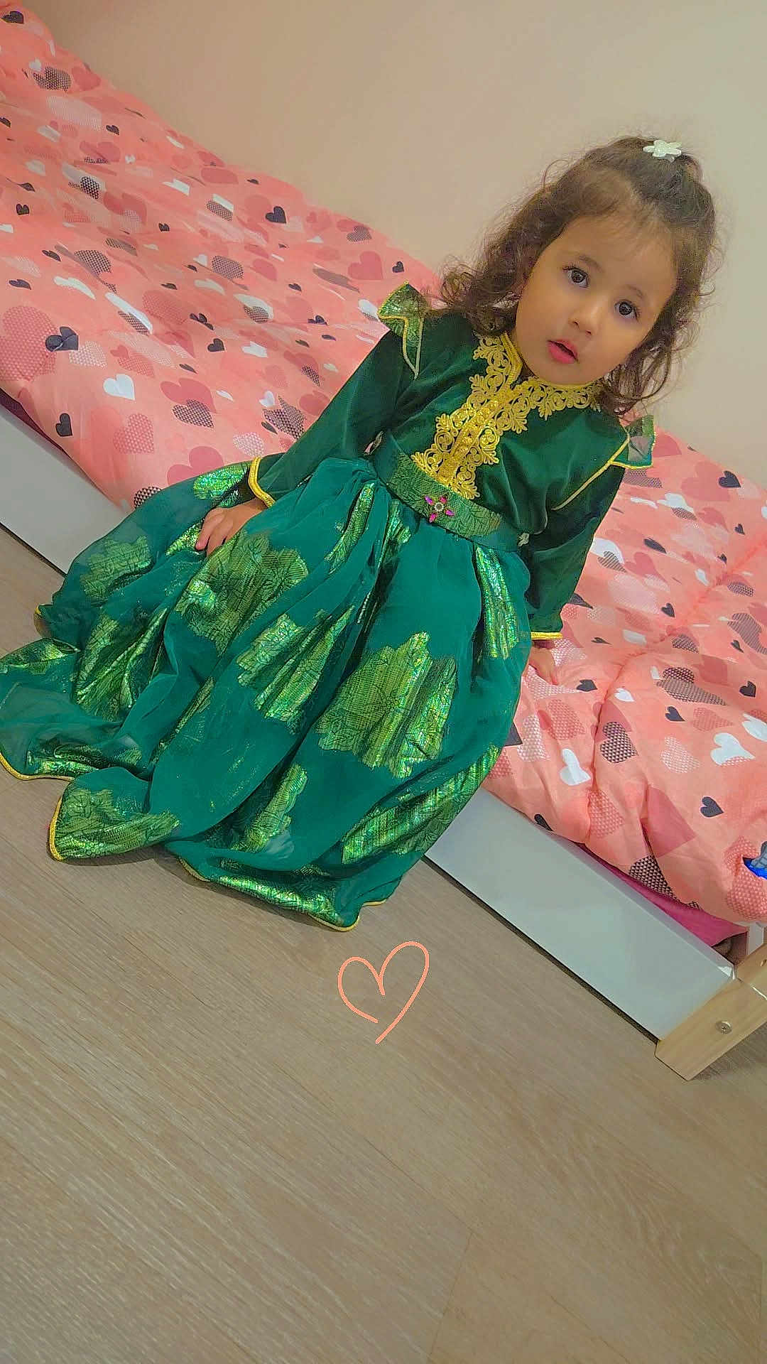 Alice a rejoint le concours — aidez-le/la à gagner de superbes lots ! child, girl, dress, green_dress, bed, pink_bedspread, heart_pattern, floor, wooden_floor, curly_hair, indoors, portrait, expression, sitting, person, decor, home, cute, young, face