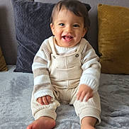 Bennaceur Maxime a rejoint le concours — aidez-le/la à gagner de superbes lots ! baby, child, smiling, couch, blanket, pillow, indoor, clothing, overalls, sweater, happy, cute, toes, feet, person, home, soft, cozy, portrait, sitting
