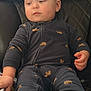 baby, child, onesie, moose_print, navy_blue, leather_chair, quilted, hand, face, sitting, indoor, curious, furniture, young_child, cozy, clothing, person, infant, soft_fabric, relaxed