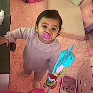 Zahya a rejoint le concours — aidez-le/la à gagner de superbes lots ! baby_clothes, child, colorful_toys, curious, cushion, cute, floor, home, indoor, infant, pacifier, pink, pink_carpet, playroom, plush, soft_toys, standing, toddler, toy_walker, young_child