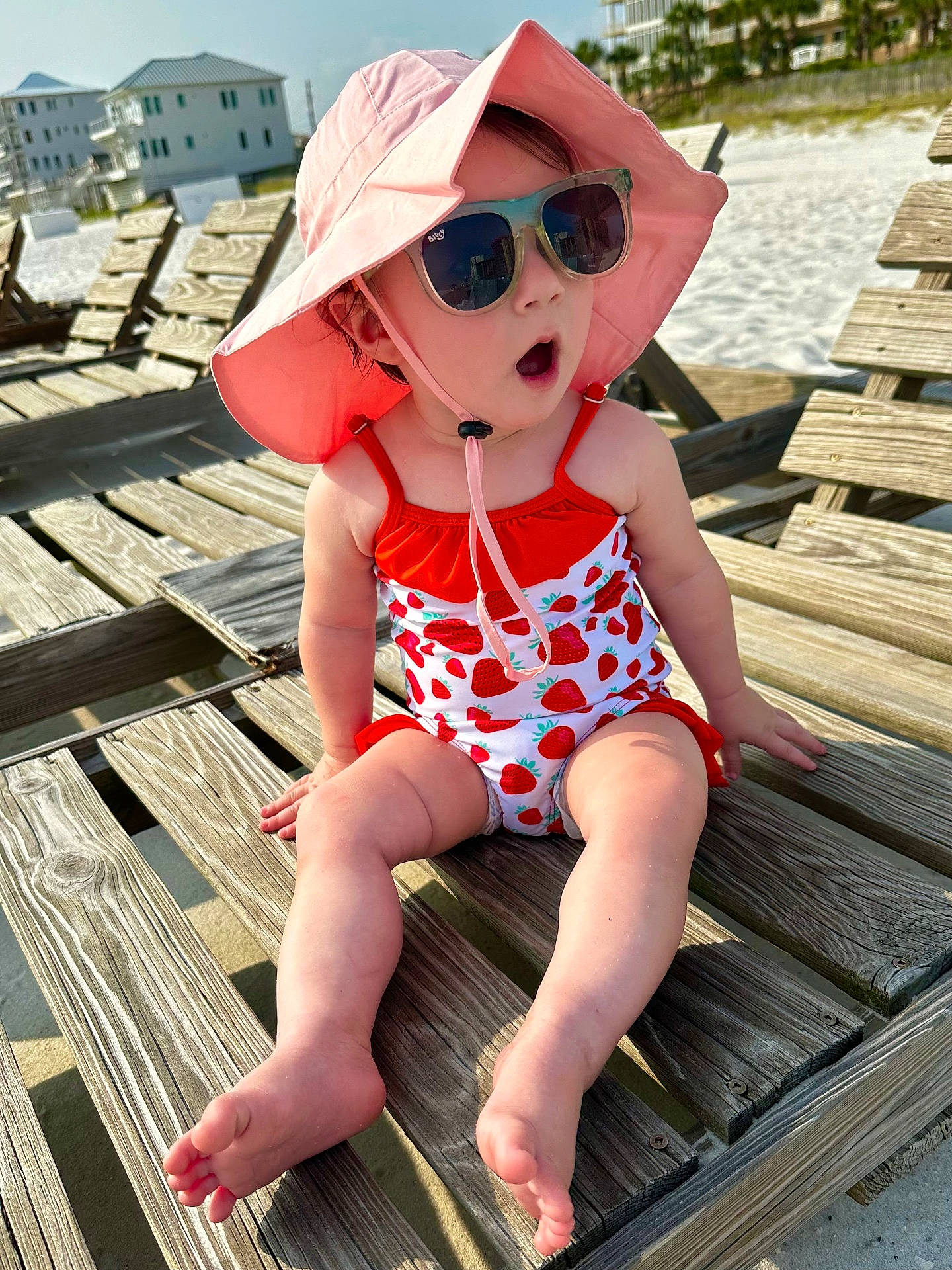 Hazel is registered to the contest to win money with this photo: accessories, architecture, baby, building, clothing, face, hat, head, outdoors, person, photography, port, portrait, shelter, sitting, summer, sunglasses, swimwear, water, waterfront