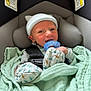 baby, newborn, pacifier, car_seat, blanket, beanie, infant, smiling, child, seatbelt, clothing, safety, cute, indoors, face, headwear, soft, wrapped, person, resting