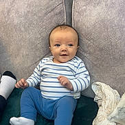 Ronnie joined the competition — help win amazing prizes! baby, infant, child, couch, cushion, striped_shirt, blue_pants, socks, smiling, indoor, person, seated, soft_furniture, blanket, cozy, cute, happy, young_child, head, face