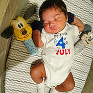 Armando is registered to the contest to win money with this photo: baby, newborn, sleeping, infant, onesie, plush_toy, mattress, pattern, socks, cute, peaceful, indoor, child, resting, soft_toys, celebration, holiday_clothing, face, hands, legs