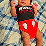 baby, infant, mickey_mouse, onesie, clothing, blanket, pattern, blue, white, red, skin, cute, lying_down, hand, face, person, newborn, soft, comfort, portrait