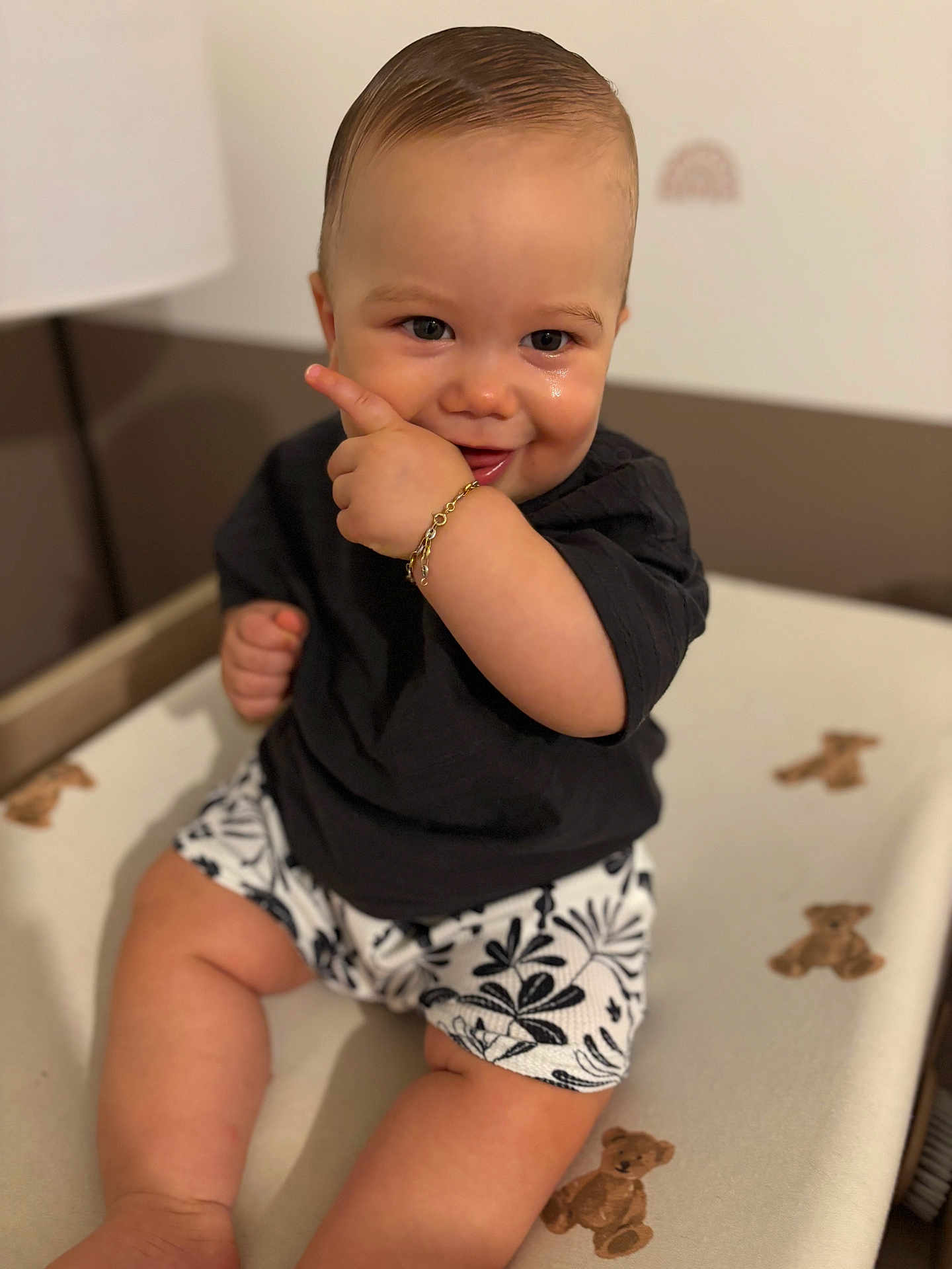 Giulio participe au concours pour gagner de l'argent avec cette photo : baby, child, smiling, pointing, black_shirt, floral_shorts, teddy_bear_pattern, changing_pad, indoors, cute, happy, skin, face, hand, sitting, short_hair, expression, infant, person, playful