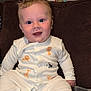 baby, child, infant, onesie, animal_print, smiling, blue_eyes, sitting, blanket, couch, indoor, happy, cute, face, young, person, soft_lighting, plush, comfort, portrait