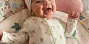 Raya is registered to the contest to win money with this photo: baby, smiling, headband, bow, infant, cushion, blanket, floral_pattern, onesie, happy, lying_down, indoors, child, cute, soft_texture, comfort, playful, joyful, face, person