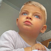 Slayven a rejoint le concours — aidez-le/la à gagner de superbes lots ! child, toddler, blonde_hair, blue_eyes, close_up, portrait, indoor, looking_up, serious_expression, sweater, skin, ear, hand, bedroom, pillow, natural_light, soft_lighting, candid, young_child, portrait_photography