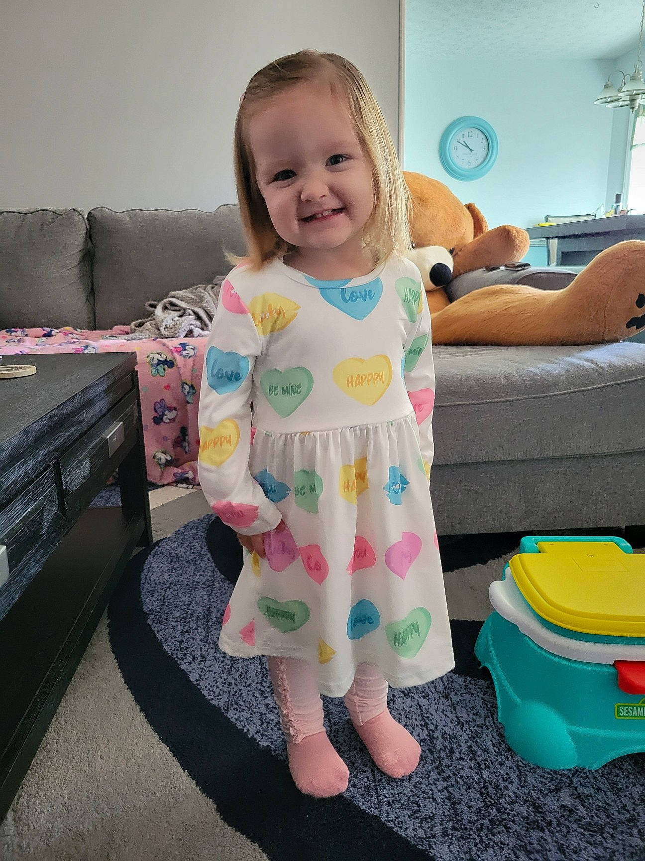 Ava is registered to the contest to win money with this photo: arm, baby, baby_toddler_clothing, child, couch, dress, floor, flooring, fun, hand, happy, joy, person, pink, product, purple, skin, sleeve, smile, standing
