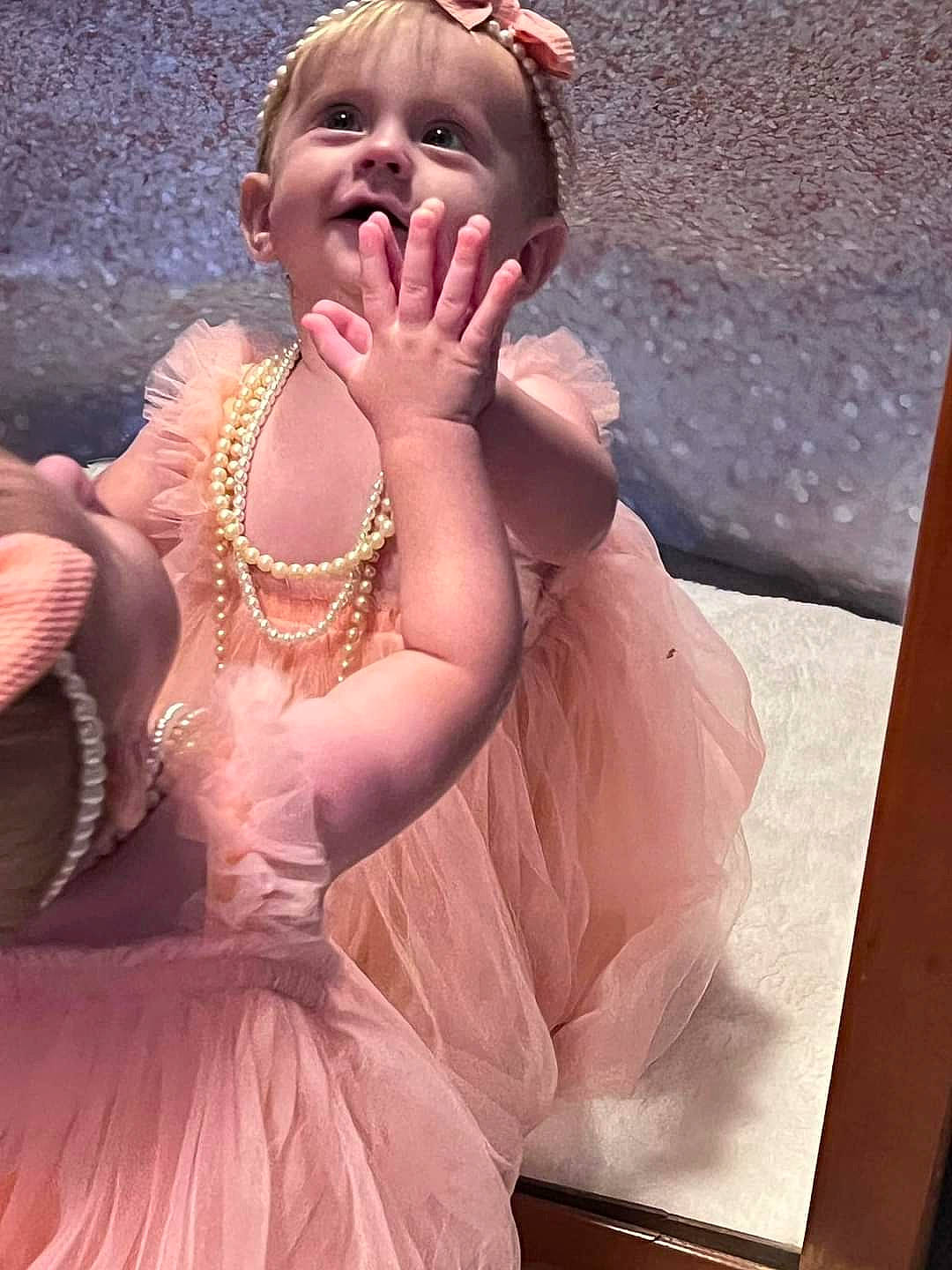 Ariella is registered to the contest to win money with this photo: abdomen, arm, baby, chest, child, event, eye, fashion_accessory, formal_wear, gesture, hand, happy, head, headgear, jewellery, person, pink, sitting, smile, toddler
