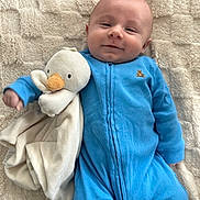 Asher is registered to the contest to win money with this photo: baby, blue_onesie, plush_toy, duck, smiling, infant, blanket, soft_texture, comfort, cute, child, face, lying_down, cozy, happy, toddler, indoors, sleepwear, person, stuffed_animal