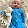 baby, blue_onesie, plush_toy, duck, smiling, infant, blanket, soft_texture, comfort, cute, child, face, lying_down, cozy, happy, toddler, indoors, sleepwear, person, stuffed_animal