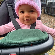 Madison joined the competition — help win amazing prizes! baby, baby_clothes, baby_seat, child, curious, cute, face, fence, gravel, green_blanket, infant, knit_hat, outdoor, person, pink_hat, portrait, seatbelt, smile, stroller, warm_clothing