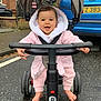 Madison joined the competition — help win amazing prizes! baby, child, pink_clothing, hooded_jacket, barefoot, tricycle, stroller, smiling, outdoor, street, wet_pavement, car, ford, blue_car, brick_house, baby_toy, happy, person, footwear_absent, handlebar