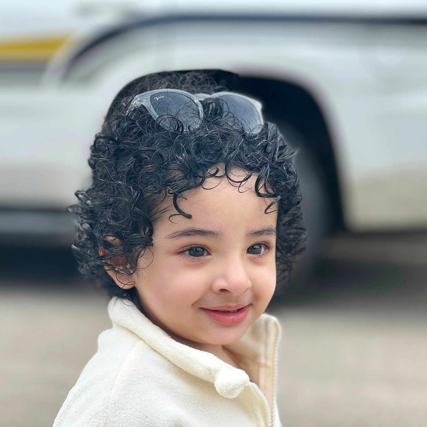 Azaan joined the competition — help win amazing prizes! child, curly_hair, sunglasses, smile, outdoor, vehicle, face, portrait, person, young, casual_clothing, innocence, cute, happy, headwear, closeup, human, daylight, expression, curiosity