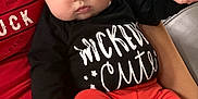 Amelia joined the competition — help win amazing prizes! baby, infant, child, person, face, black_shirt, orange_pants, sitting, couch, indoor, cute, chubby_cheeks, hand, arm, clothing, portrait, looking, eyes, human, holding