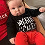 baby, infant, child, person, face, black_shirt, orange_pants, sitting, couch, indoor, cute, chubby_cheeks, hand, arm, clothing, portrait, looking, eyes, human, holding