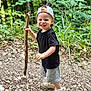 Soan a rejoint le concours — aidez-le/la à gagner de superbes lots ! child, toddler, boy, smiling, cap, black_tshirt, gray_shorts, white_shoes, stick, forest, outdoor, nature, rocks, path, greenery, playful, happy, walking, summer, casual_clothing
