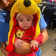 Adonis joined the competition — help win amazing prizes! baby, child, adult, winnie_the_pooh, hat, red_clothing, yellow_hat, store, clothing_rack, shopping, indoor, person, portrait, cute, holding, face, headwear, expressionless, hands, casual
