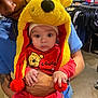 baby, child, adult, winnie_the_pooh, hat, red_clothing, yellow_hat, store, clothing_rack, shopping, indoor, person, portrait, cute, holding, face, headwear, expressionless, hands, casual