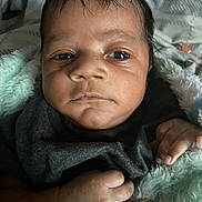 Josiah is registered to the contest to win money with this photo: baby, infant, face, hand, blanket, clothing, newborn, skin, portrait, closeup, curious, soft_texture, indoor, sleepwear, cuddly, cute, person, child, natural_light, resting