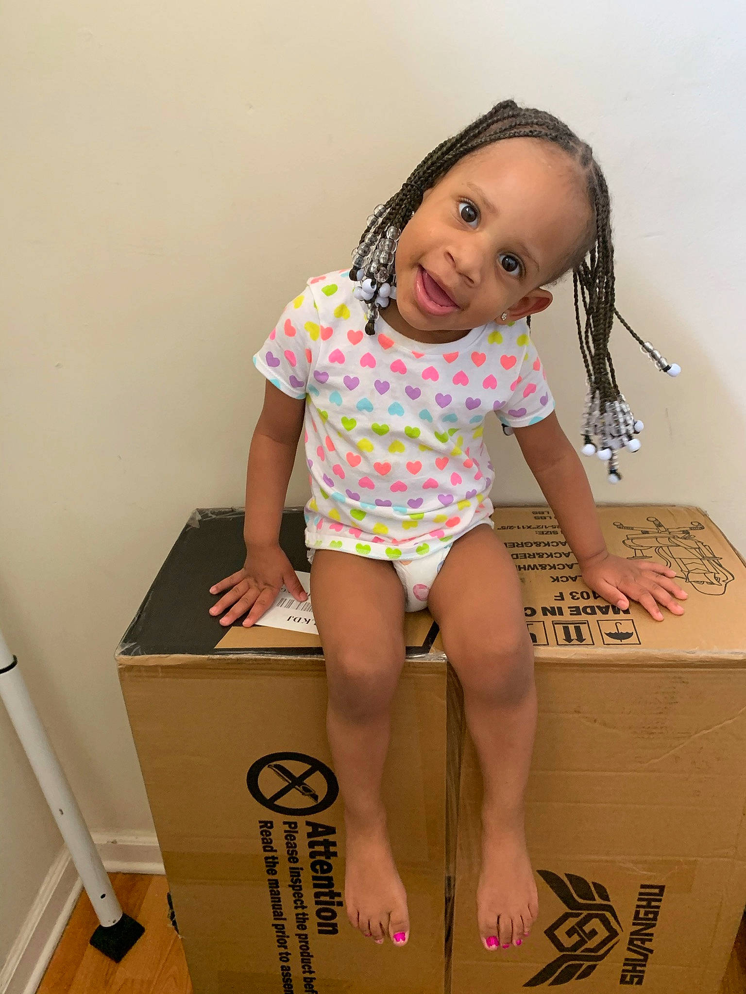 Rylee is registered to the contest to win money with this photo: baby_toddler_clothing, box, carton, finger, flash_photography, fun, happy, human_leg, neck, one_piece_garment, packaging_and_labeling, packing_materials, pattern, person, shipping_box, sitting, sleeve, smile, standing, thigh