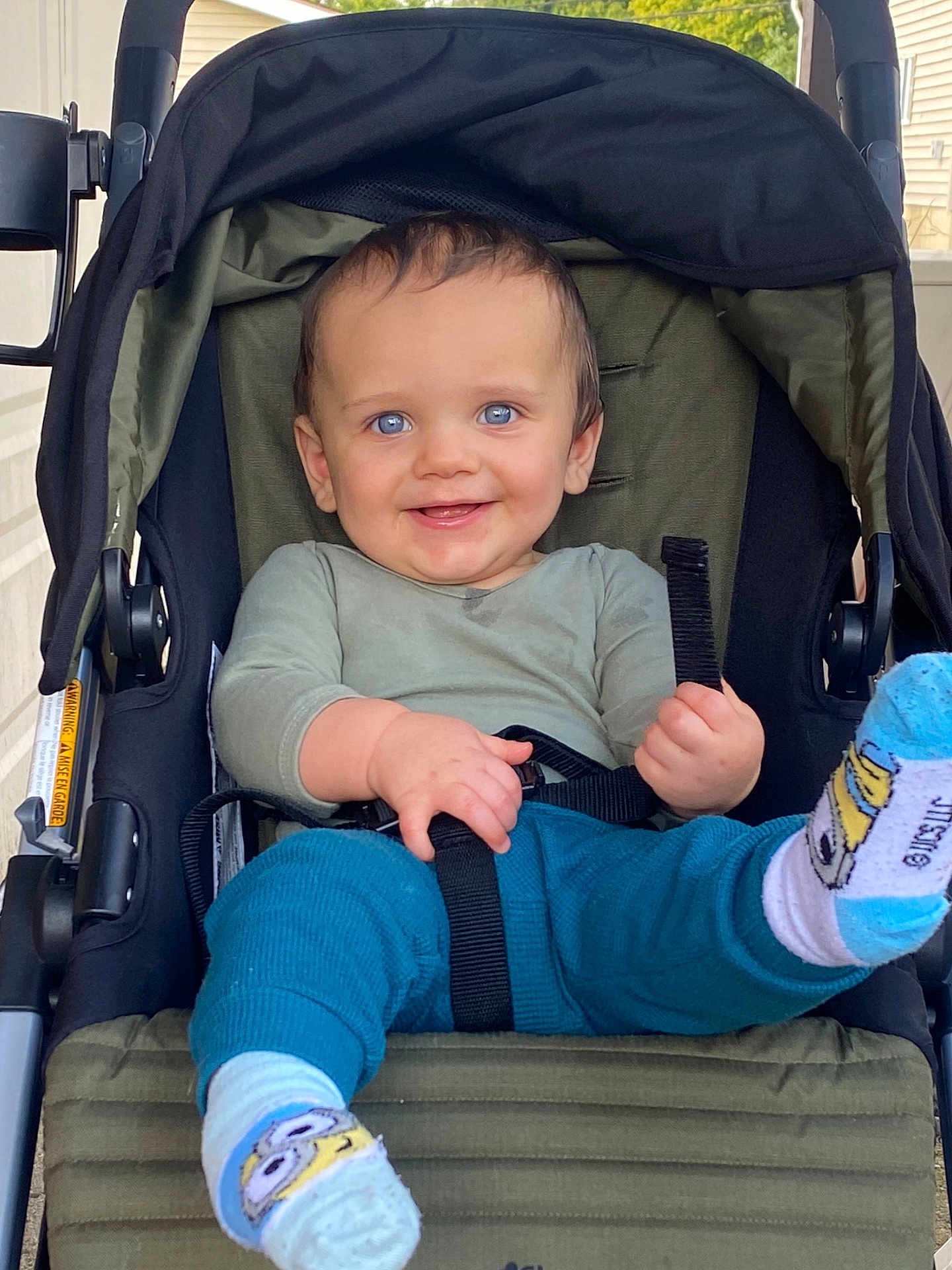 Jacob is registered to the contest to win money with this photo: baby, child, stroller, smiling, blue_eyes, socks, minions, clothing, happy, portrait, infant, seatbelt, hand, footwear, outdoor, urban, person, cute, casual, playful