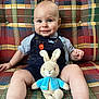 baby, plush_toy, bunny, couch, plaid, child, smiling, blue_eyes, shorts, striped_shirt, indoor, seated, cute, toy, soft_toy, button, fabric, pattern, happy, person