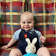 Johnny joined the competition — help win amazing prizes! baby, child, smiling, plush_toy, bunny, overalls, striped_shirt, couch, plaid_pattern, colorful, indoor, seated, happy, cute, toy, person, face, furniture, comfort, portrait