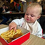 Nansi joined the competition — help win amazing prizes! toddler, child, french_fries, chicken_nuggets, food, box, table, bib, sweater, indoor, restaurant, people, colorful_banners, hand, curious, eating, high_chair, blond_hair, casual, dining