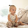 Piper is registered to the contest to win money with this photo: toddler, child, bed, stuffed_animal, toy, indoor, portrait, blond_hair, pony_tail, casual_clothing, white_bed, soft_light, cute, baby, relaxed, home, comfort, daylight, sitting, person