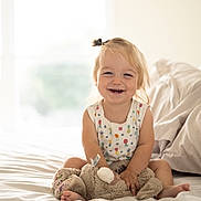 Piper joined the competition — help win amazing prizes! toddler, child, smiling, bed, stuffed_animal, plush_toy, indoor, natural_light, pony_tail, happy, cute, person, clothing, white_bedspread, soft_toys, infant, sitting, cozy, home, portrait