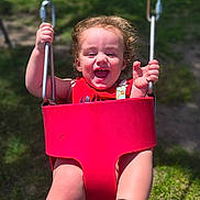 Johnathan joined the competition — help win amazing prizes! toddler, child, swing, playground, outdoor, happy, smiling, curly_hair, red_swing, sunlight, grass, holding, fun, joy, baby, person, clothing, footwear, summer, play