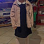 Gabryelle a rejoint le concours — aidez-le/la à gagner de superbes lots ! child, smiling, indoor, tiled_floor, jacket, dress, tights, sneakers, person, furniture, television, shelf, clutter, toy, happy, standing, floor, casual_clothing, hair, young