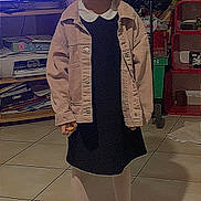 Gabryelle participe au concours pour gagner de l'argent avec cette photo : child, smiling, indoor, tiled_floor, jacket, dress, tights, sneakers, person, furniture, television, shelf, clutter, toy, happy, standing, floor, casual_clothing, hair, young