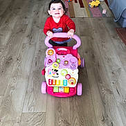 Hisae a rejoint le concours — aidez-le/la à gagner de superbes lots ! child, toddler, baby, toy_walker, pink_toy, red_shirt, smiling, indoor, wood_floor, colorful_rug, toys, sofa, playroom, carpet, wheels, flooring, happy, living_room, portrait, activity_toy