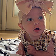 Rosalee joined the competition — help win amazing prizes! baby, child, headband, bow, blanket, pattern, indoor, curious, face, blue_eyes, plaid_dress, mouth_open, skin, hand, floor, door, light, natural_light, expression, infant