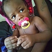 Keeayla is registered to the contest to win money with this photo: toddler, child, pacifier, braids, beads, curious, person, arm, tattoo, pink_shirt, indoor, closeup, hands, skin, face, expression, seated, comfort, adult, holding